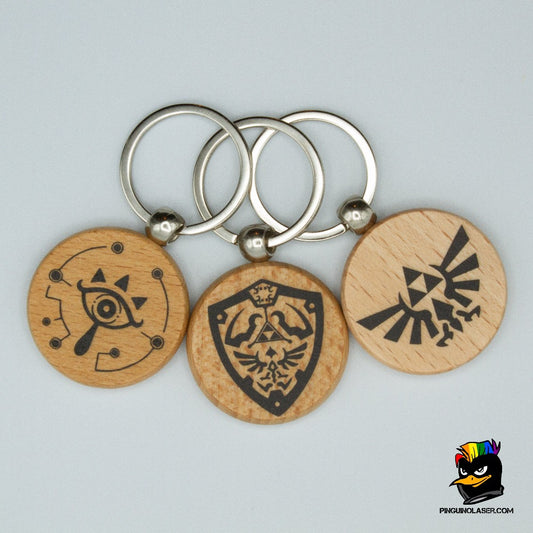 Foto de conjunto de tres llaveros redondos de madera natural con motivos del videojuego Zelda. De izquierda a derecha: símbolo Sheikah, Escudo Hyliano y Familia Real.