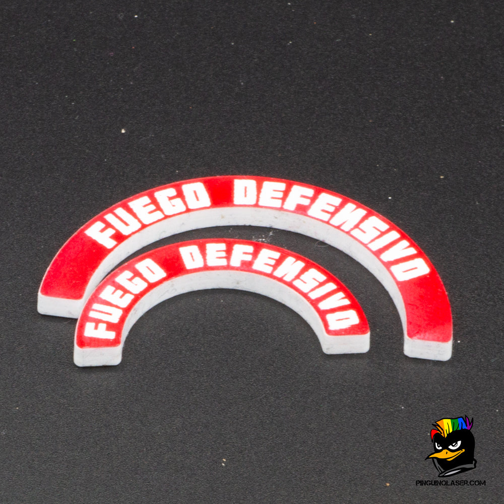 Dos marcadores de metacrilato con el texto "fuego defensivo" en tipología de Punkapocalyptic. El de arriba es para peanas de 40mm y el de abajo para peanas de 25mm. Son de color rojo con las letras en blanco. Se ponen junto a la peana, ya que la forma curvada de los marcadores se ajusta a la circunferencia de la misma.