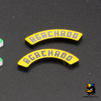 Dos marcadores de metacrilato con el texto "Agachado" en tipología de Punkapocalyptic. El de arriba es para peanas de 40mm y lde abajo para peanas de 25mm. Son de color amarillo con las letras en color negro. Se ponen junto a la peana, ya que la forma curvada de los marcadores se ajusta a la circunferencia de la misma. 