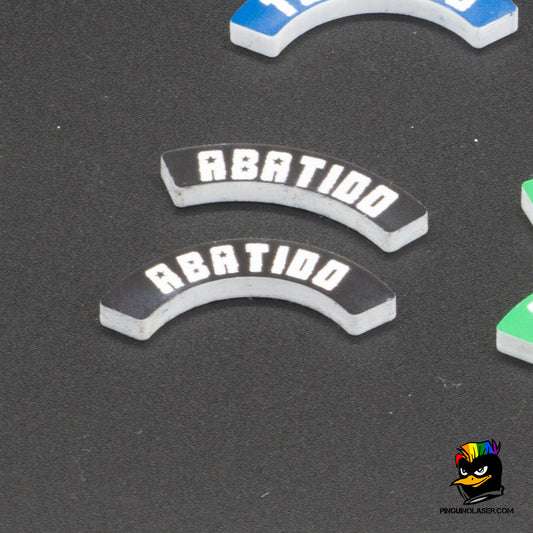 Dos marcadores de metacrilato con el texto "Abatido" en tipología de Punkapocalyptic. El de arriba es para peanas de 40mm y el de abajo para peanas de 25mm. Son de color negro con el texto en blanco. Se ponen junto a la peana, ya que la forma curvada de los marcadores se ajusta a la circunferencia de la misma.