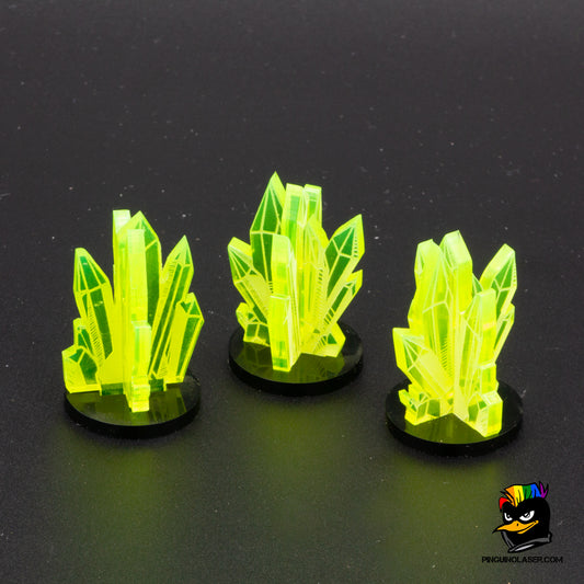Foto de tres marcadores de la misión "corazón verde". Hechos en metacrilato verde fluorescente, tienen forma de cristales minerales apilados entre sí en una peana negra de metacrilato. 