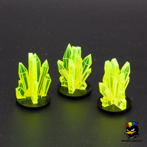 Foto de tres marcadores de la misión "corazón verde". Hechos en metacrilato verde fluorescente, tienen forma de cristales minerales apilados entre sí en una peana negra de metacrilato. 