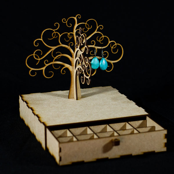Joyero de madera en forma de árbol sin hojas con un cajón como base. El cajón está abierto y se ve que tiene pequeñas separaciones. En un de las ramas hay unos pendientes colgados.