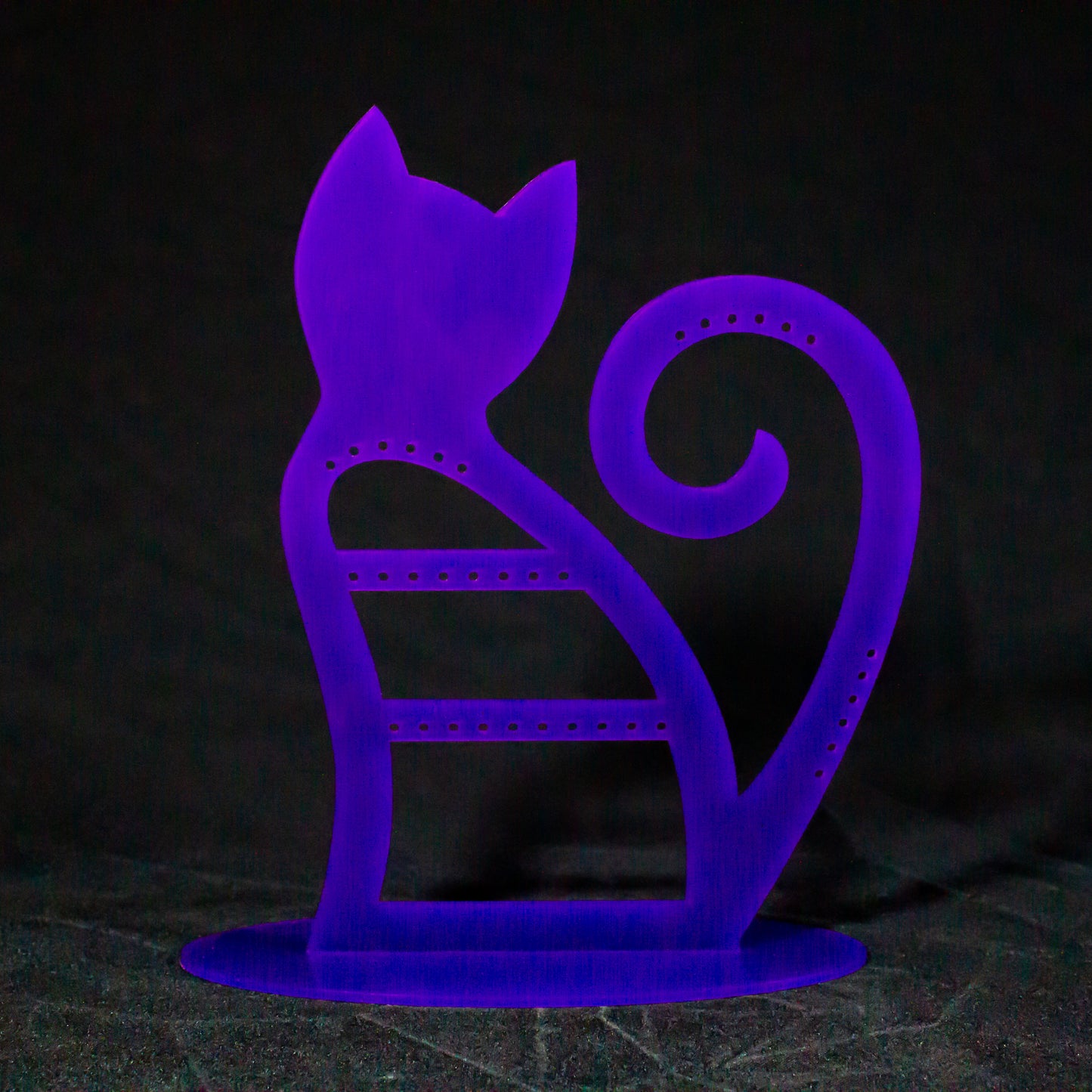 Joyero expositor en color morado con forma degato de espaldas con la cola levantada y enrollada sobre sí misma. Tiene agujeros para pendientes en la zona del cuerpo, la parte alta de la cola y un lateral de ésta.