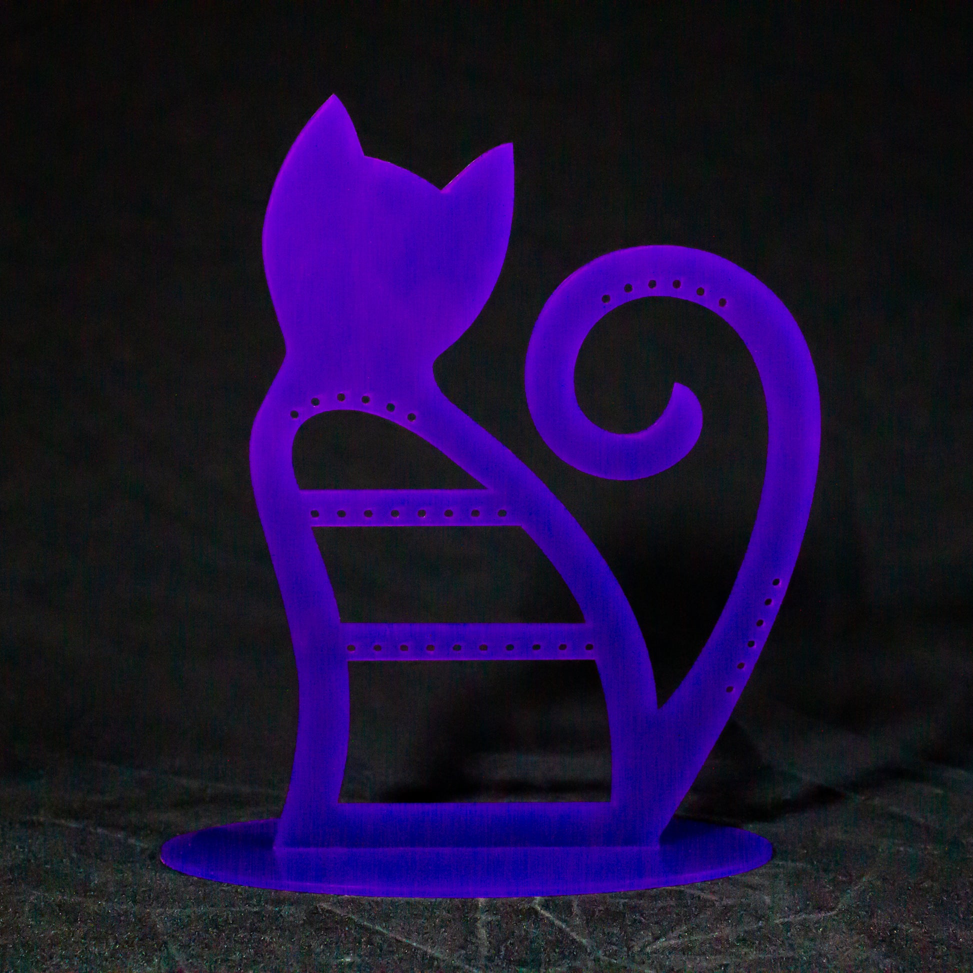 Joyero expositor en color morado con forma degato de espaldas con la cola levantada y enrollada sobre sí misma. Tiene agujeros para pendientes en la zona del cuerpo, la parte alta de la cola y un lateral de ésta.