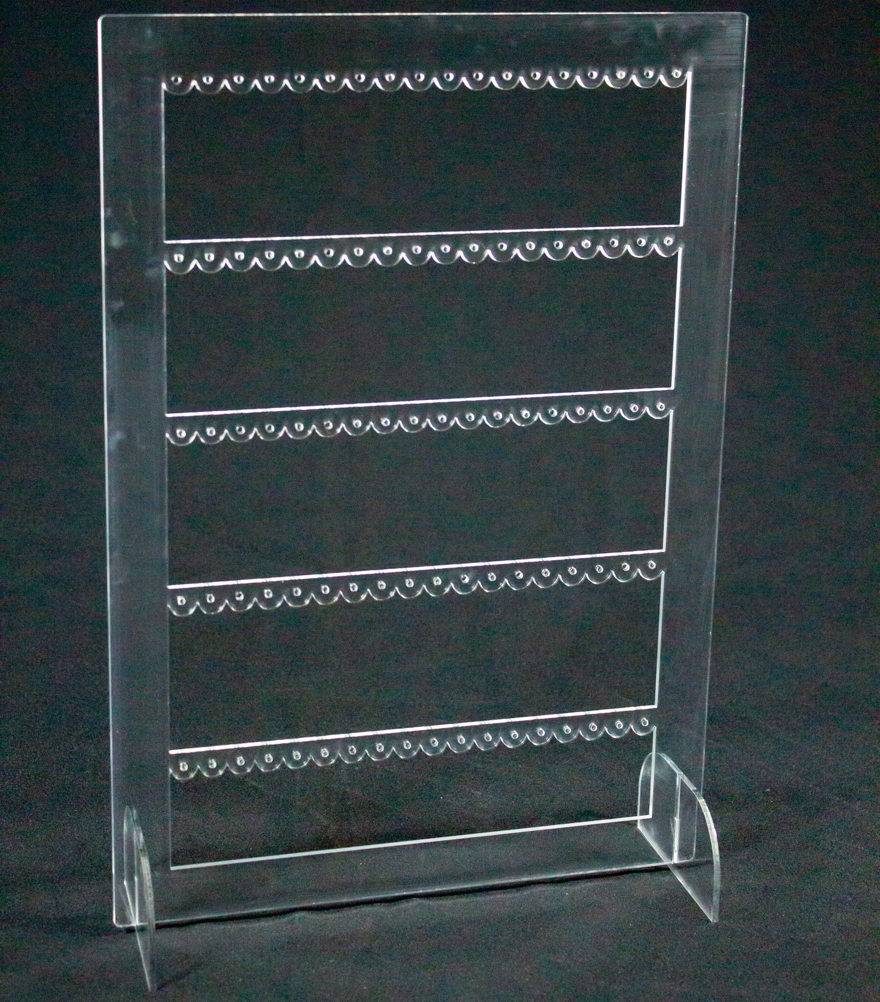 Joyero expositor para pendientes en metacrilato transparente. Es un rectángulo con tres filas en el interior con agujeros para colocar pendientes. 