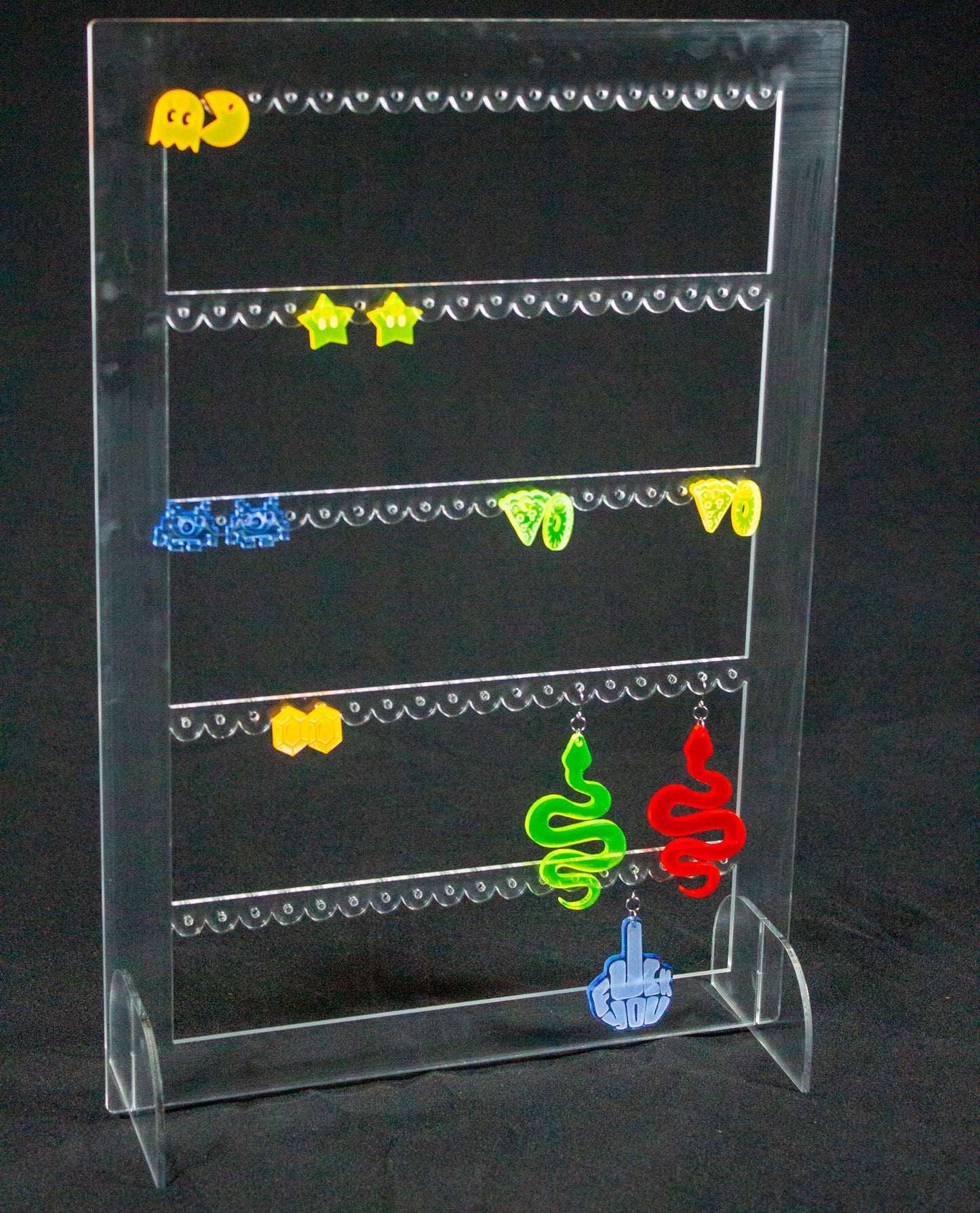 Joyero expositor para pendientes en metacrilato transparente. Es un rectángulo con tres filas en el interior con agujeros para colocar pendientes. Hay varios pendientes colgados.