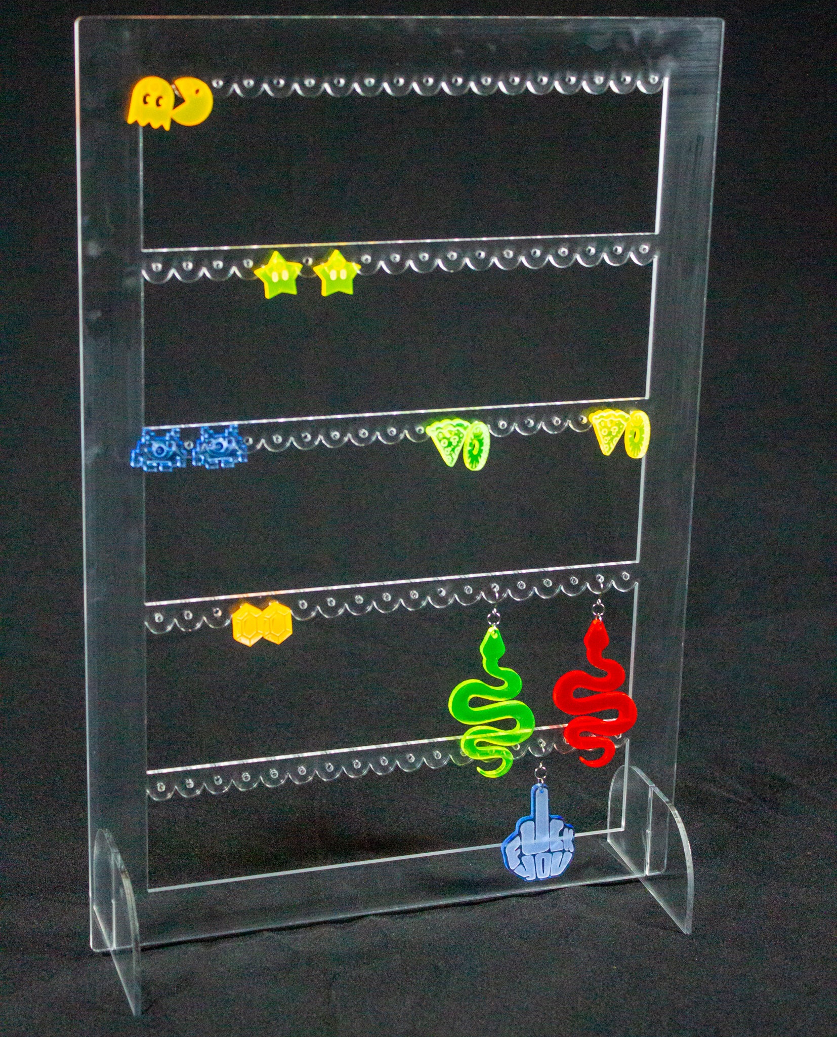 Joyero expositor para pendientes en metacrilato transparente. Es un rectángulo con tres filas en el interior con agujeros para colocar pendientes. Hay varios pendientes colgados.