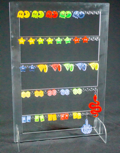 Joyero expositor para pendientes en metacrilato transparente. Es un rectángulo con tres filas en el interior con agujeros para colocar pendientes. Hay varios pendientes colgados.